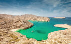 Beautiful green, blue lagoon with a small hidden beach between the harsh rocky coastal landscape at the Gulf of Oman Rocky Coast. 
